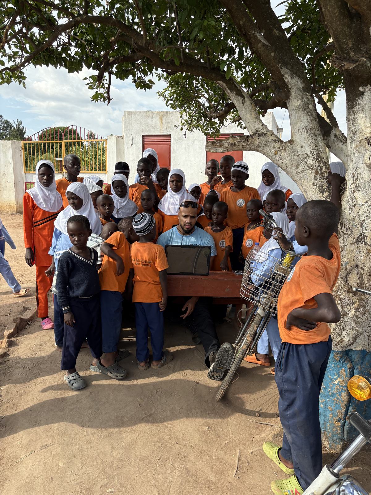 Pupils and staff gathered together under a tree on the school grounds