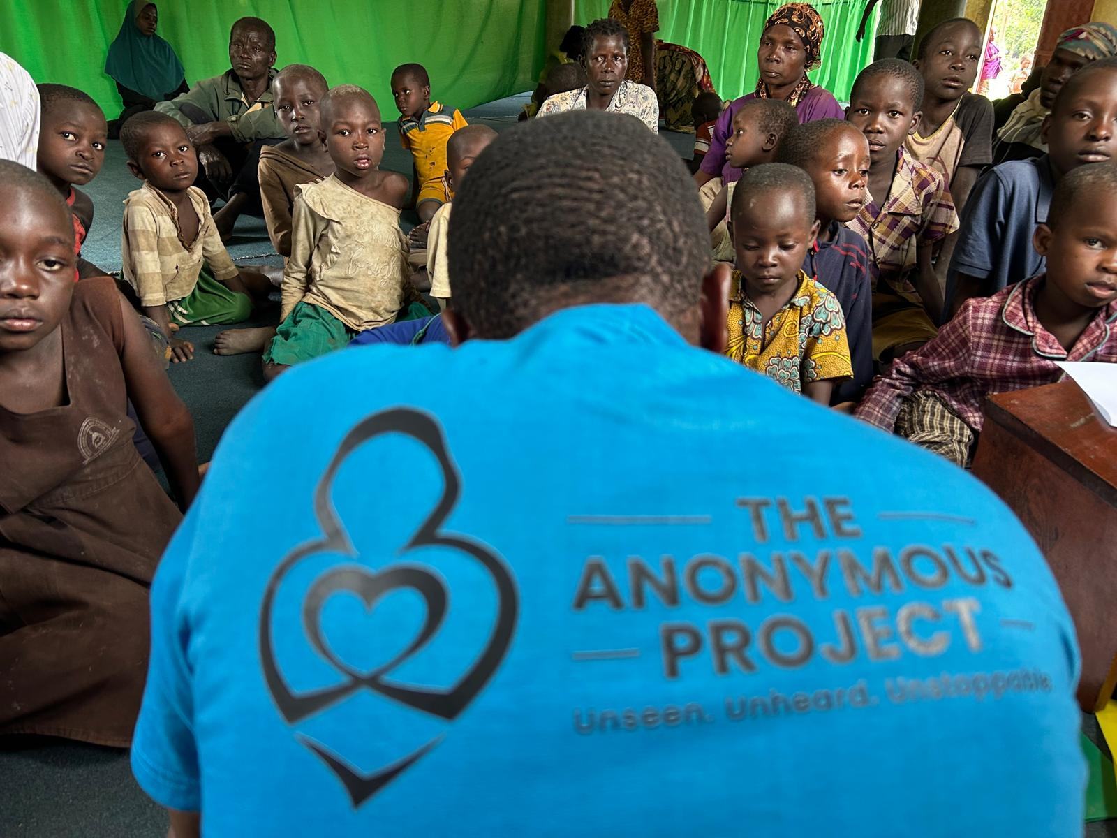 A volunteer from The Anonymous Project sitting with a group of children